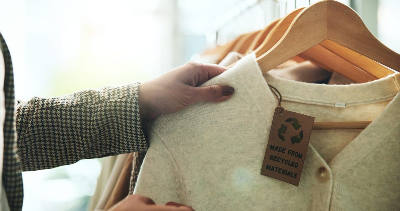 A hand holding a garment tag reading made from recycled materials
